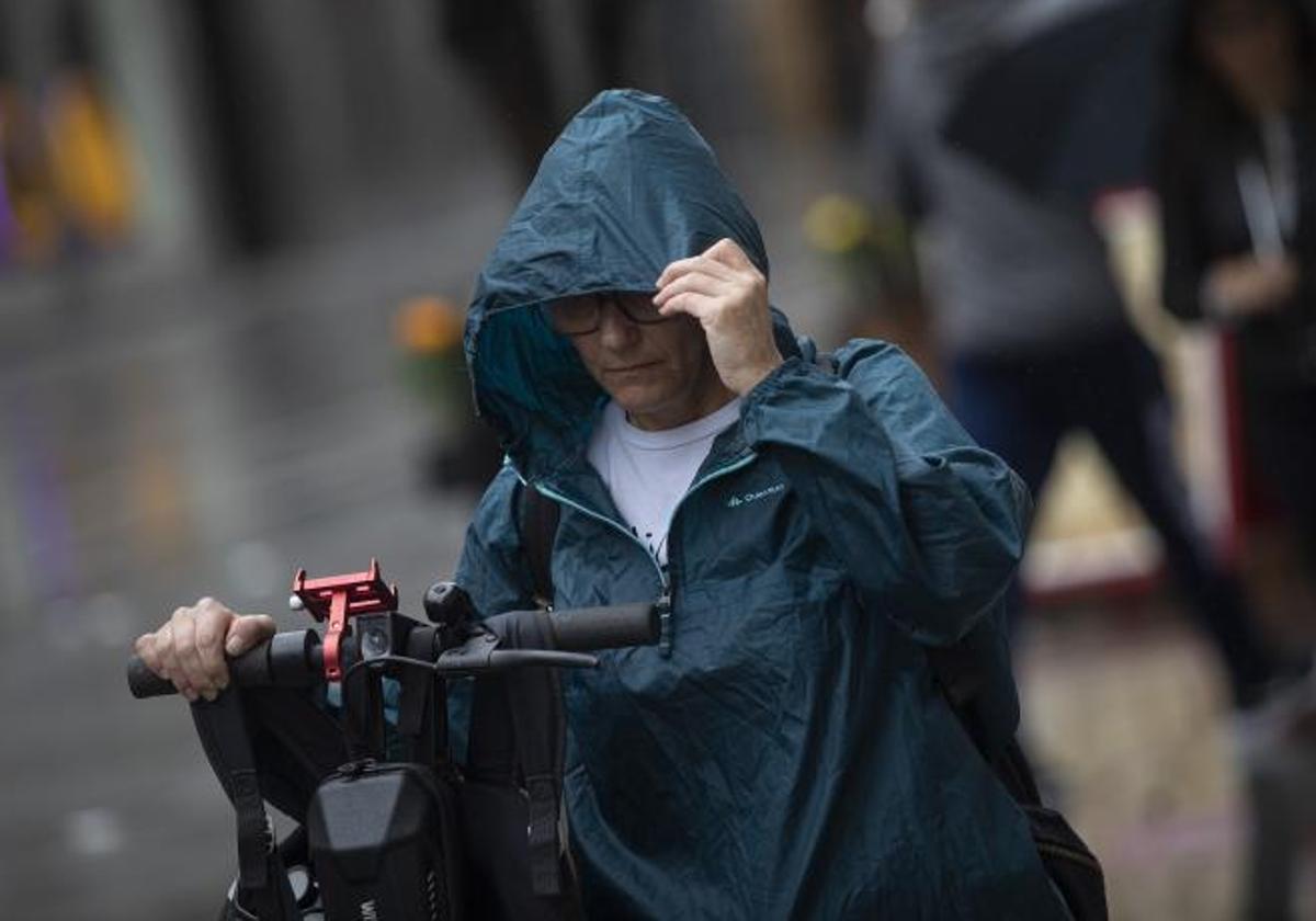 Una mujer se coloca la capucha para protegerse de la lluvia.