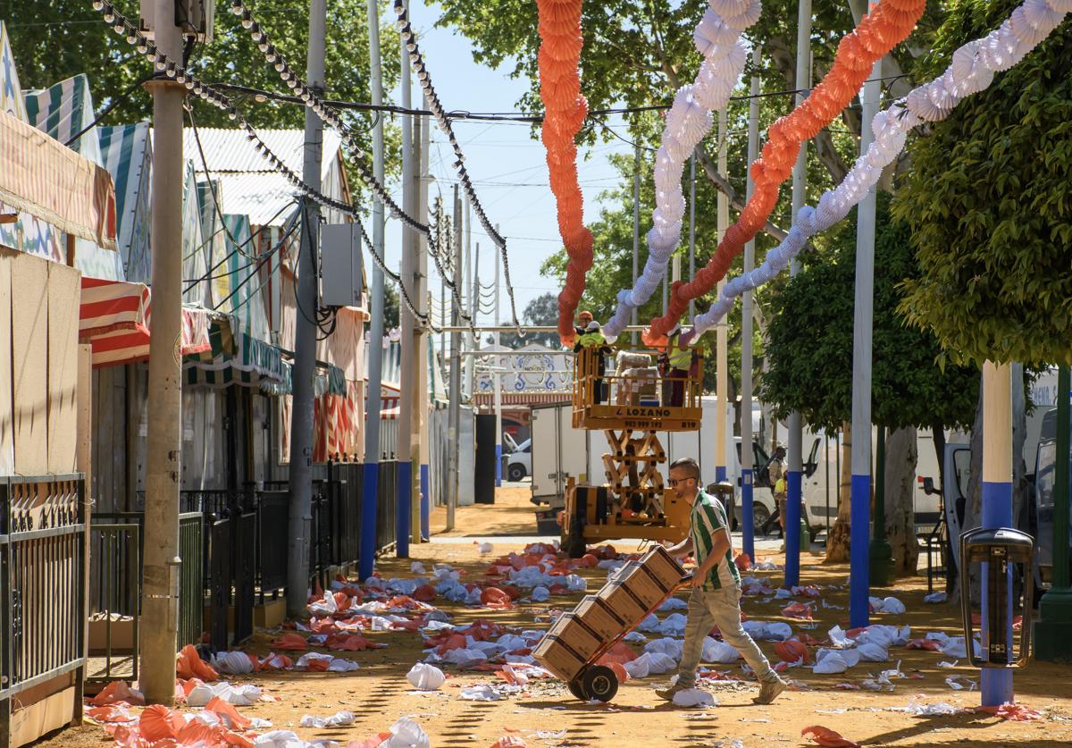 Un repartidor entre los farolillos destrozados a causa de un fuerte aguacero caído este lunes en la Feria de Sevilla