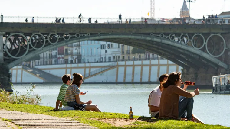 Varias personas pasan un agradable rato a orillas del río Guadalquivir, junto al Puente de Triana