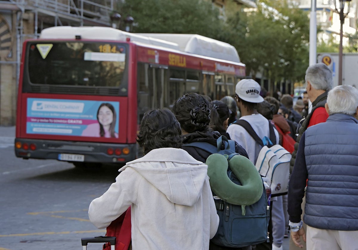 Un grupo de viajeros de Tussam esperan al autobús en la parada de la Campana