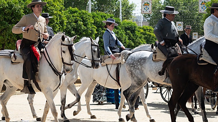 Jinetes y amazonas sobre caballos por una de las calles del Real de la Feria de Sevilla