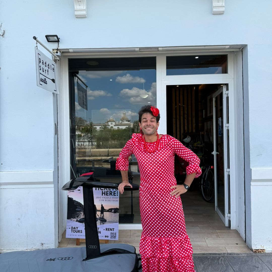 El jefe de Paddle Surf Sevilla vestido de flamenca en la puerta de su comercio