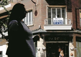 Una mujer camina delante de un piso que está a la venta