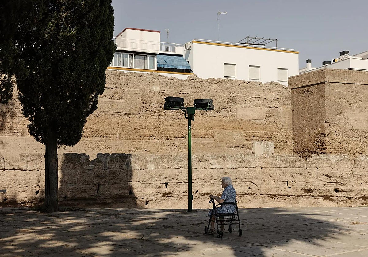 Una señora descansa a la sombra junto a la muralla de la Macarena