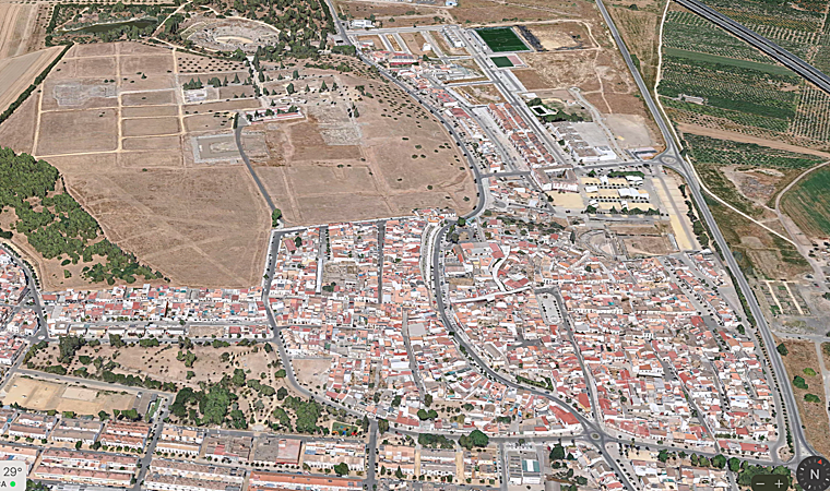 Vista aérea del conjunto urbano de Santiponce en primer plano, asentado sobre la antigua Vetus Urbs de Itálica. Al fondo, el yacimiento arqueológico con el anfiteatro y la Nova Urbs, la gran ampliación monumental de época imperial