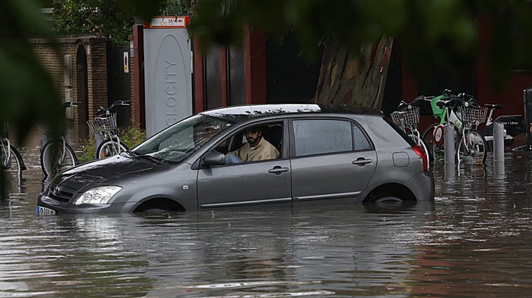 Imagen de un coche intentando circular por una calle inundada en Sevilla