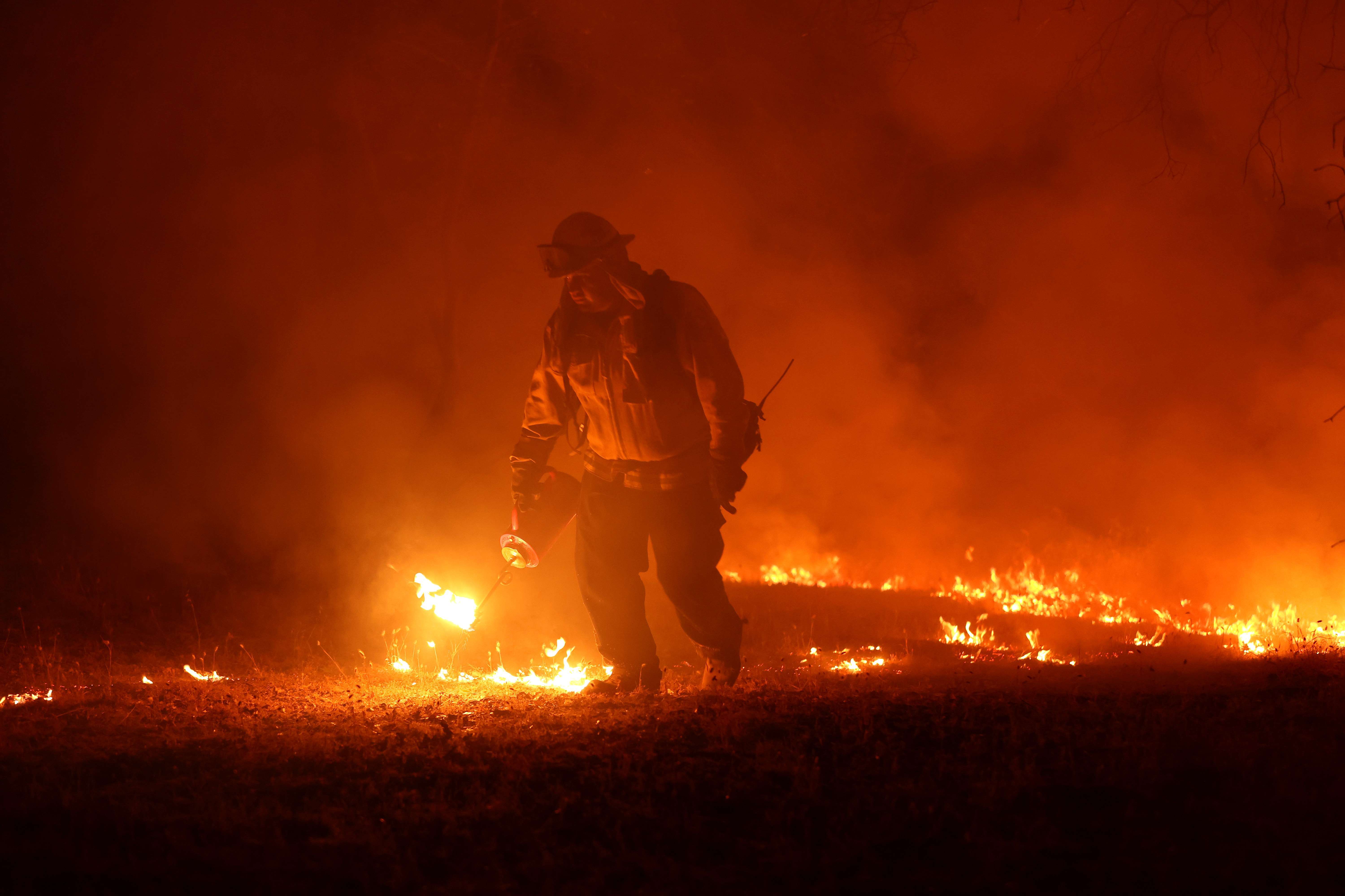 Un bombero camina entre pequeñas llamas.