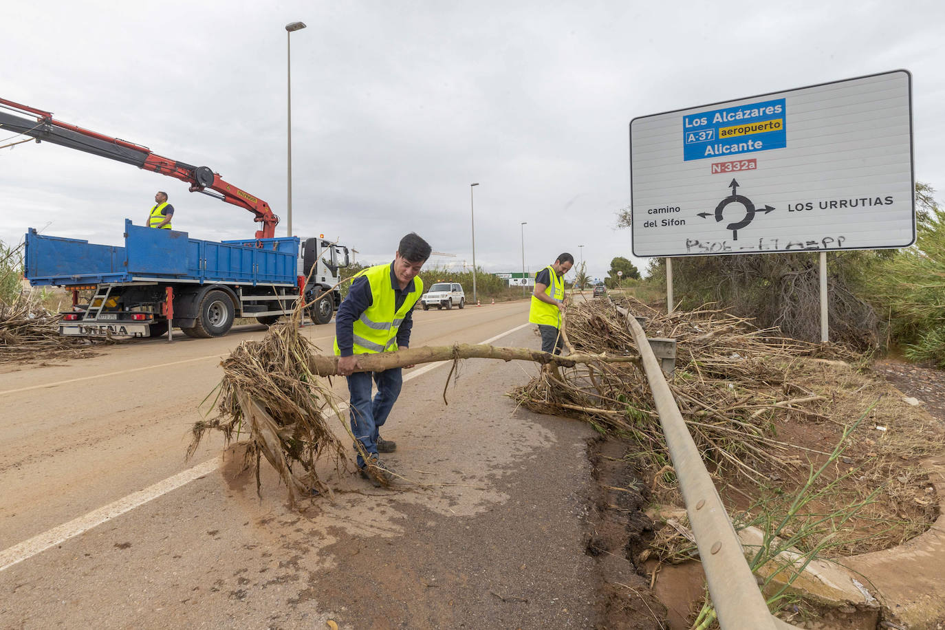 Dos operarios retiran un árbol de la carretera cortada al tráfico junto a la la rambla del Miedo en los Urrutias