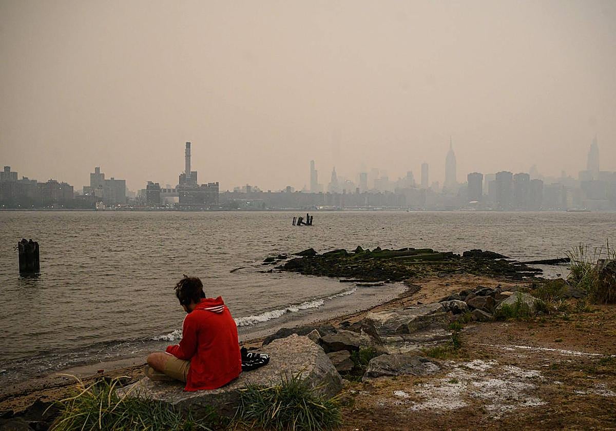 Un hombre sentado junto al río Hudson en medio del humo que cubre Nueva York por los incendios de Canadá