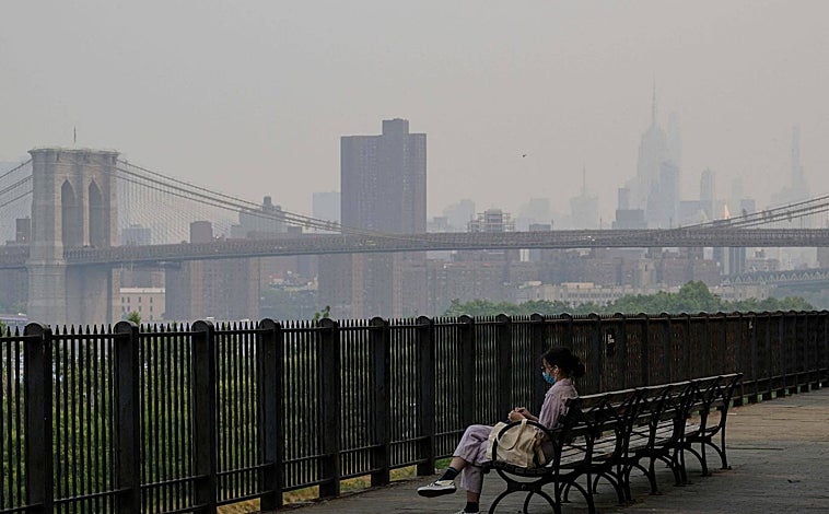Imagen principal - Varias personas permanecen en un parque mientras el horizonte de Nueva York se cubre de bruma y humo procedentes de Canadá