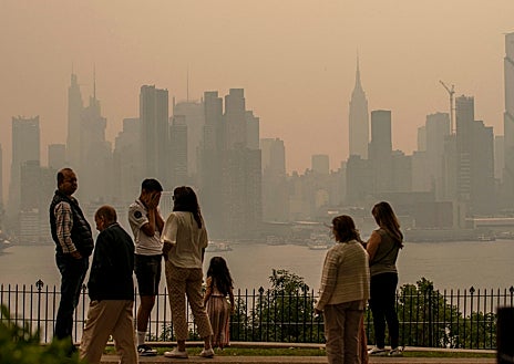 Imagen secundaria 1 - Varias personas permanecen en un parque mientras el horizonte de Nueva York se cubre de bruma y humo procedentes de Canadá