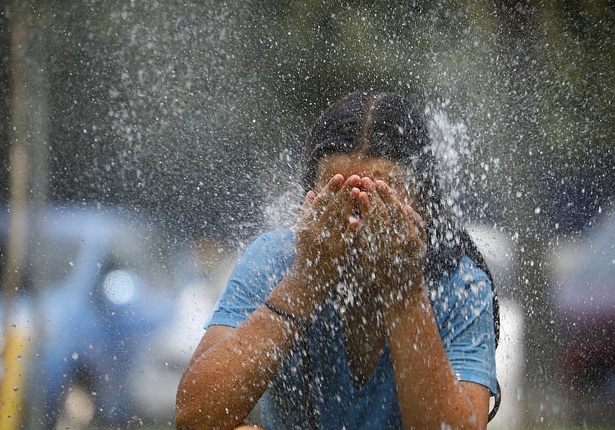 Fotografía de archivo de una joven mojándose en una fuente pública debido al calor