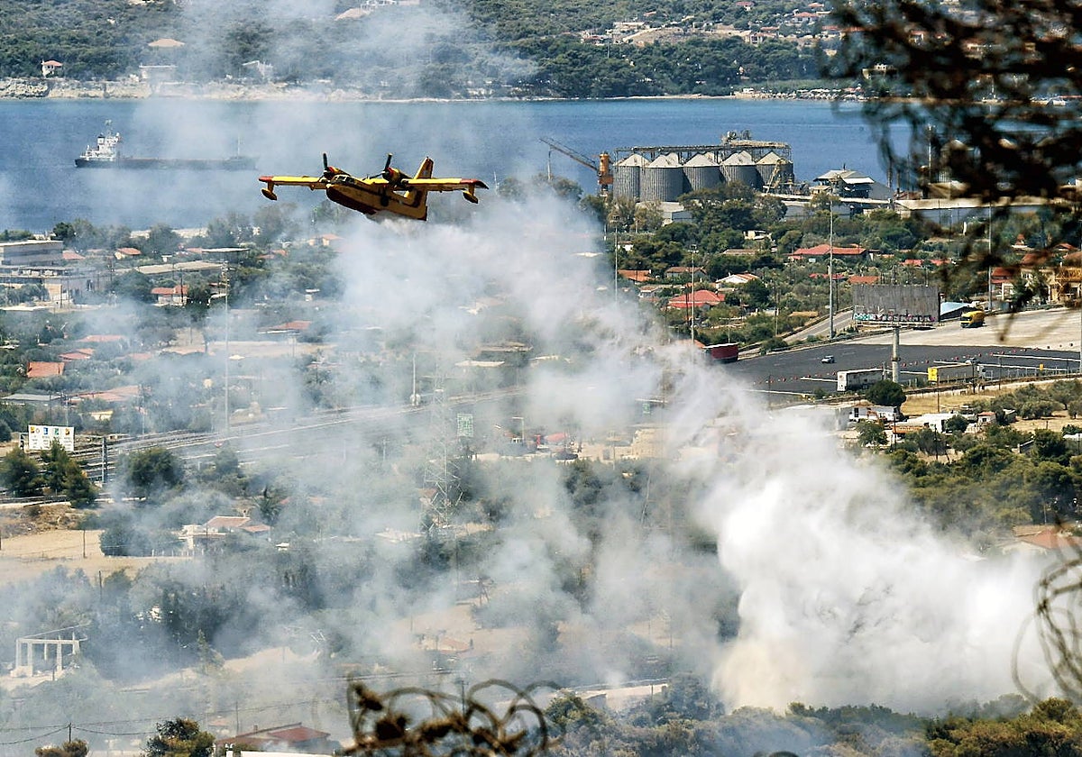 Un avión de bomberos lanza agua para extinguir un incendio forestal que está quemando una zona forestal frente a las instalaciones de la refinería Motor Oil, cerca de Lutraki, Grecia