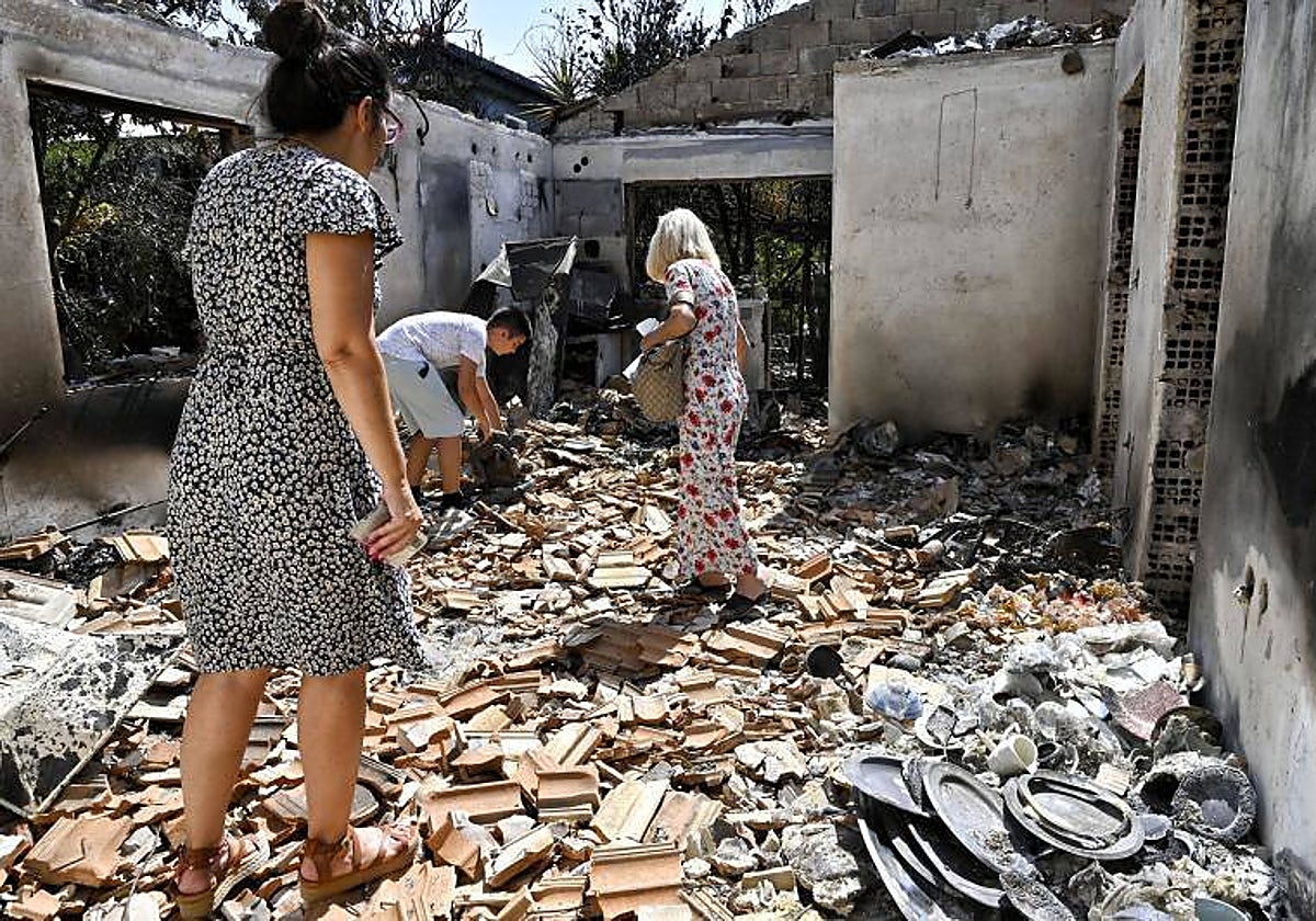 Residentes buscan entre los escombros de su casa quemada después de un incendio forestal en el área de Agia Irini, en Loutraki, Grecia