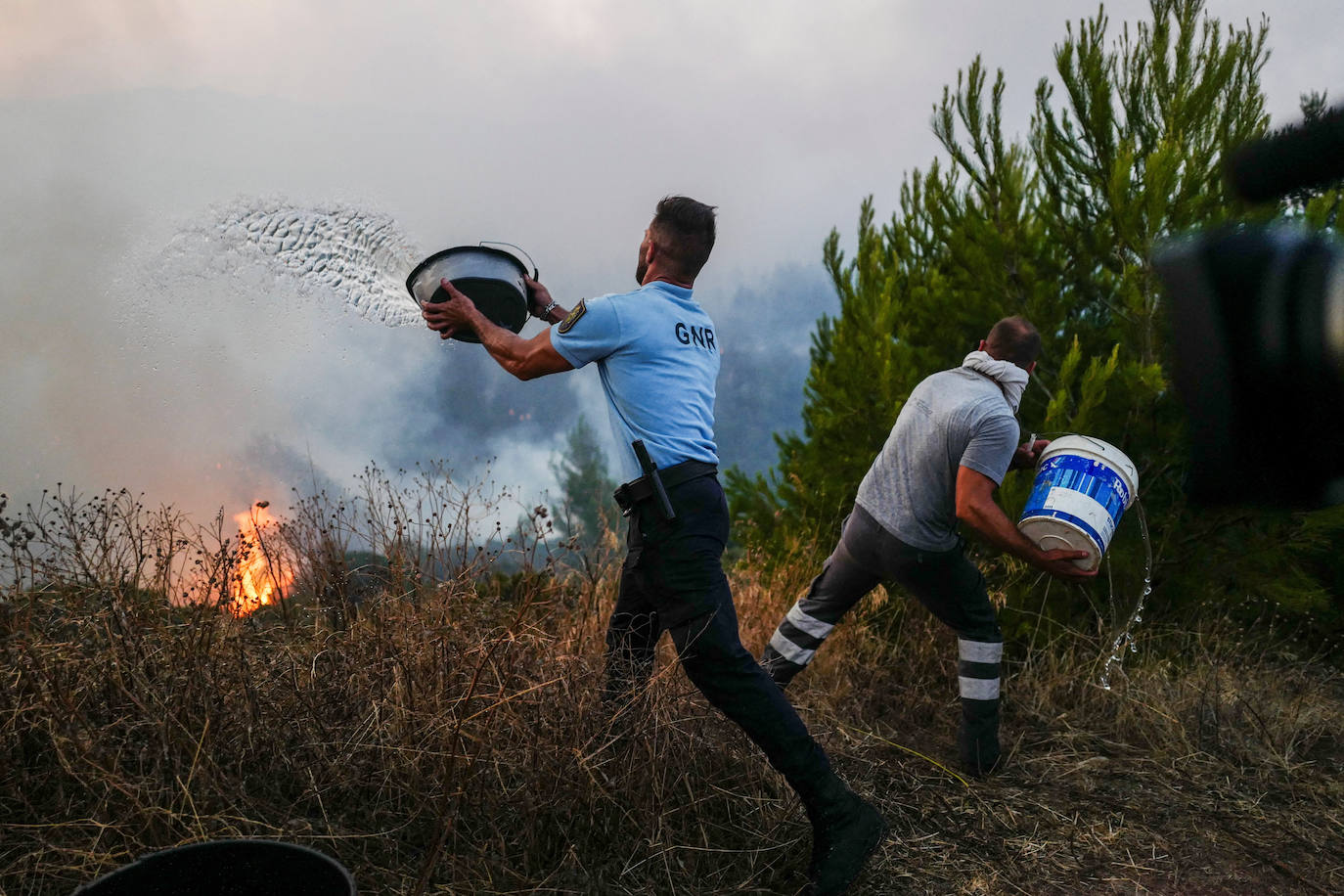 Un agente de policía y un residente local lanzan cubos de agua durante un incendio forestal en Cascais, Portugal