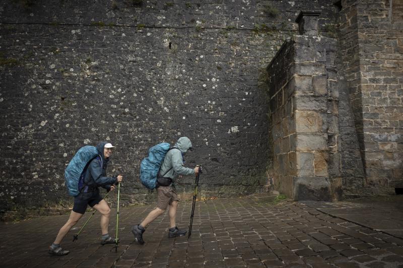 Dos peregrinos que realizan el Camino de Santiago llegan a Pamplona por el Portal de Francia en una jornada en la que la DANA está protagonizando el día