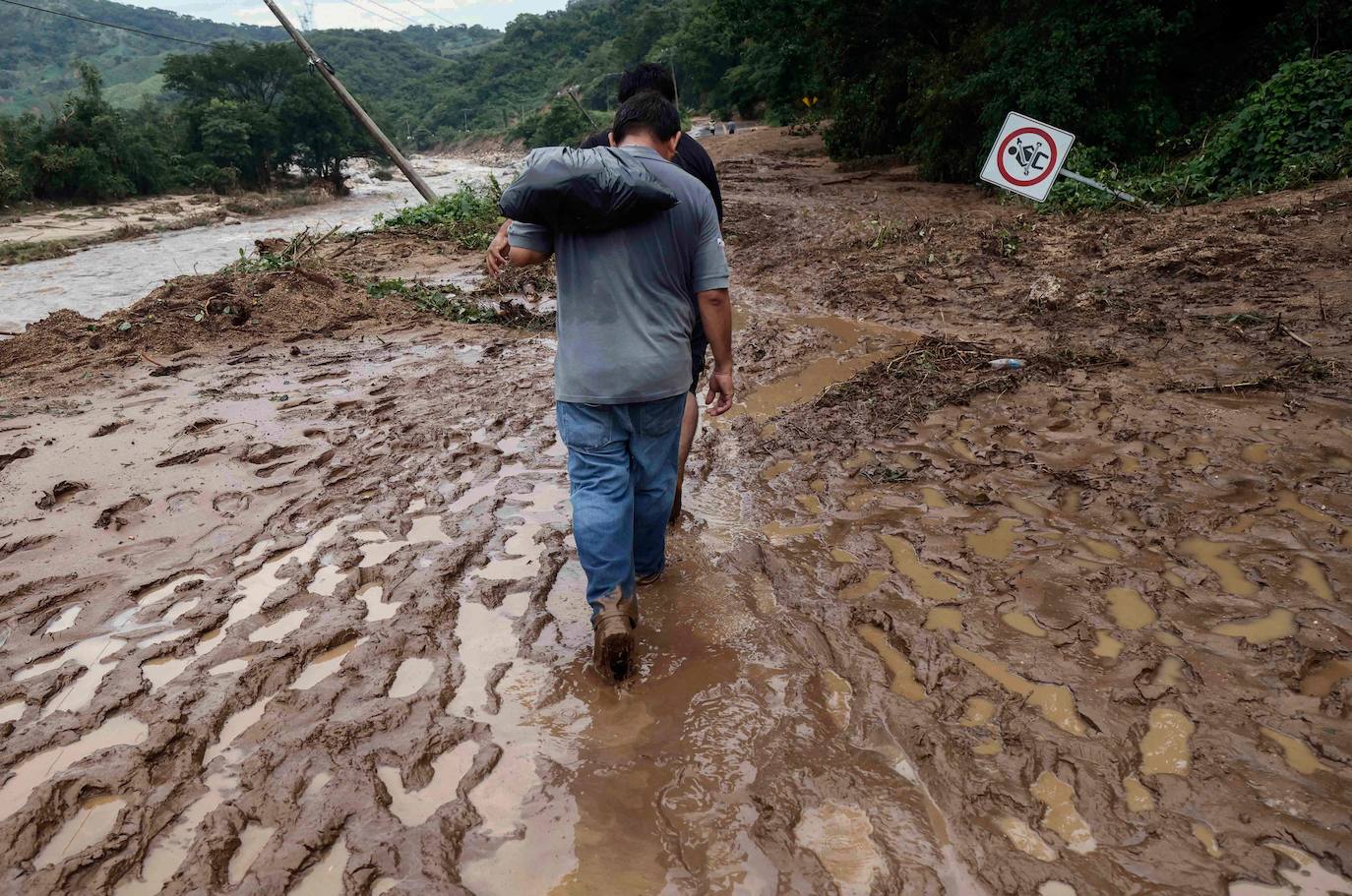 Personas caminan entre el lodo que cubre un camino en la comunidad Kilómetro 42, cerca de Acapulco