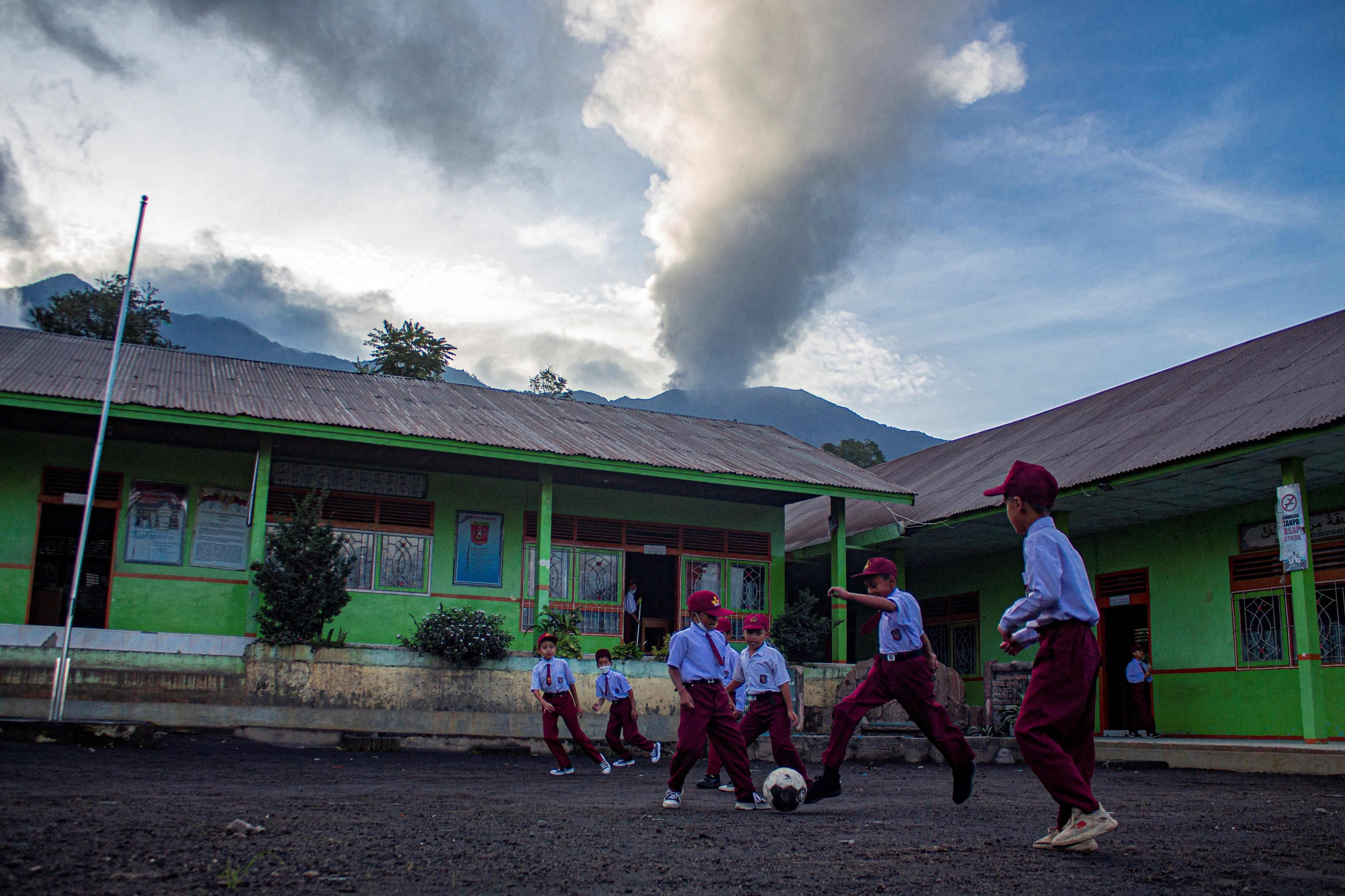 Unos niños juegan al fútbol a la vista de la columna de humo del volcán
