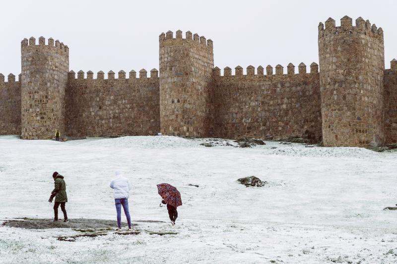 Tres personas caminan bajo la nieve en el lienzo norte de la muralla de Ávila