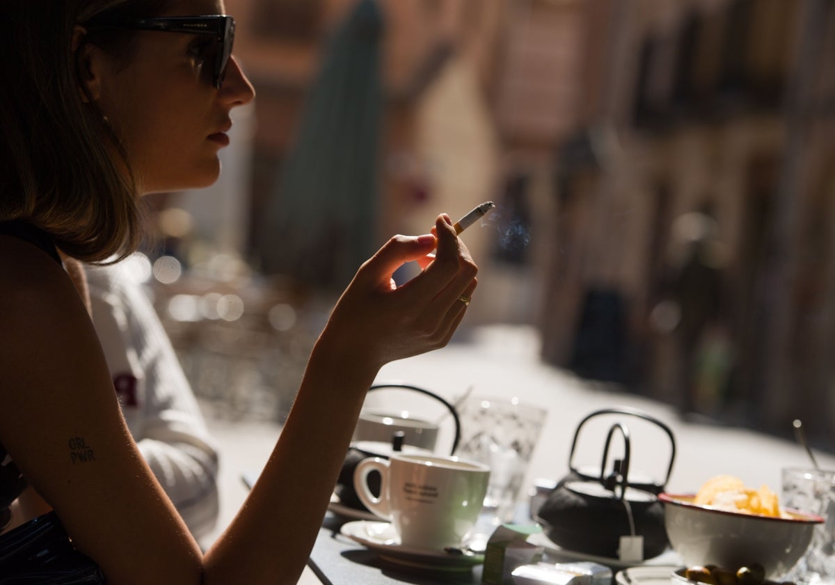 Una mujer fuma un cigarrillo en la terraza de un bar