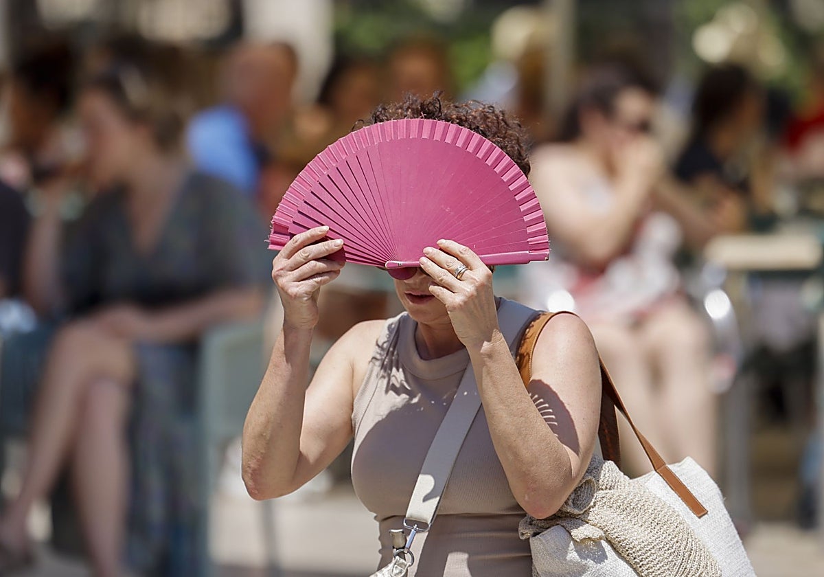 Una mujer se protege con un abanico del sol y del calor