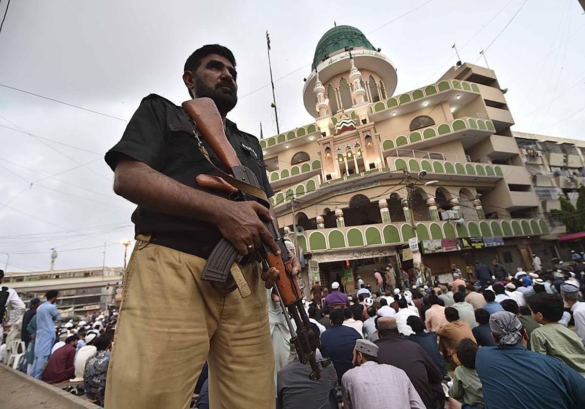Un policía vigila a la gente mientras reza en Pakistán.