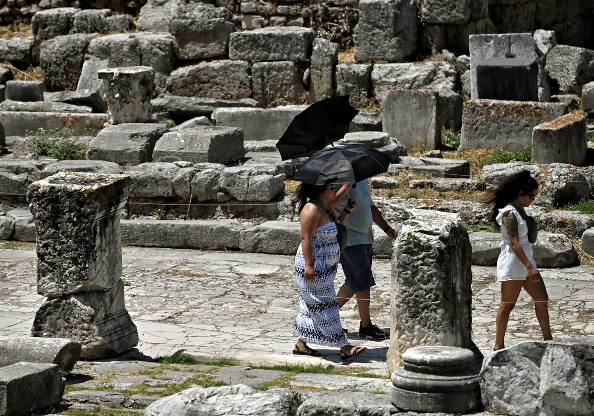 Unos turistas se protegen del sol con sombrillas en su visita a la antigua ciudad de Corinto (Grecia)