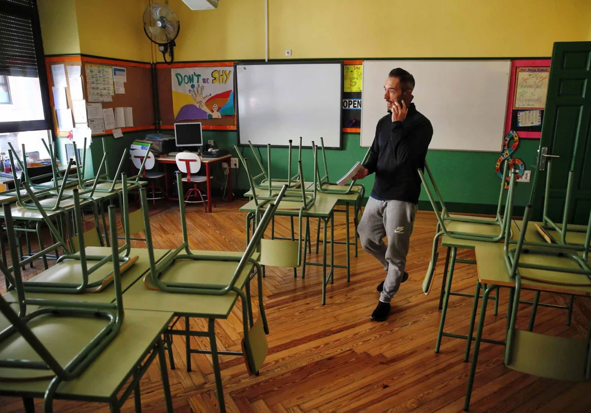 Un docente habla por su teléfono móvil en un aula desierta