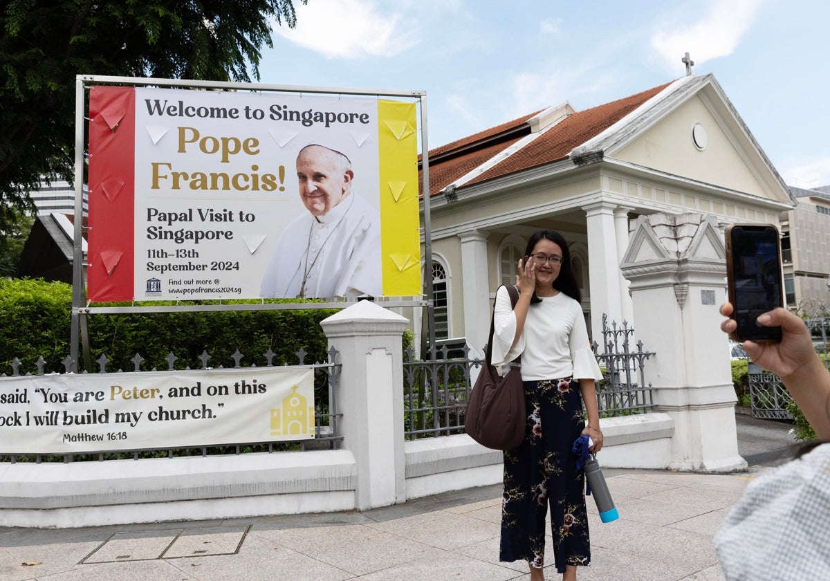 Mujer posando enfrente de un cartel que da la bienvenida al Papa en Singapur. En el vídeo, cientos de feligreses dan la bienvenida al Pontífice a Singapur.