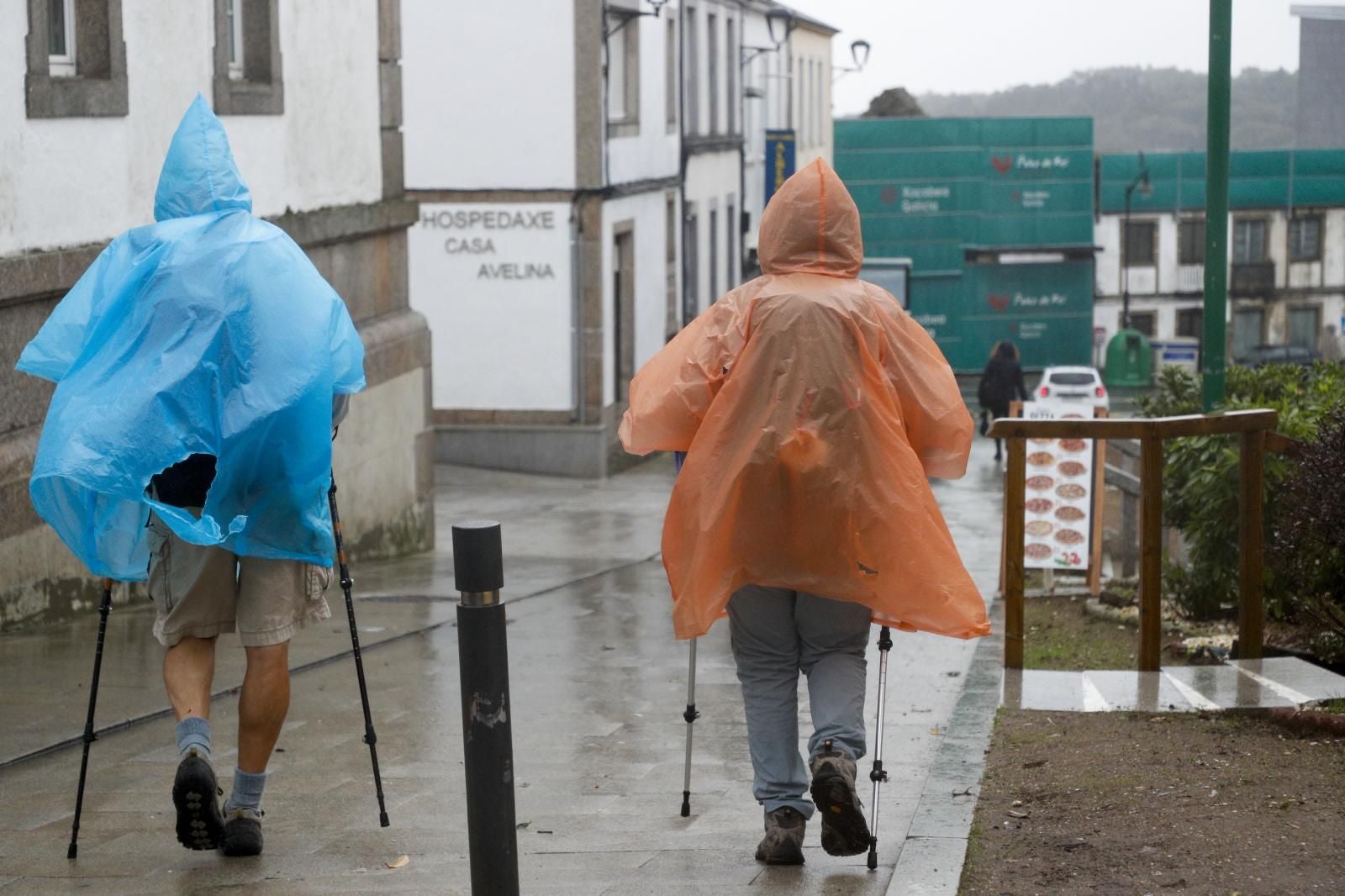 Varios peregrinos se protegen del viento y la lluvia este miércoles en Palas de Rei