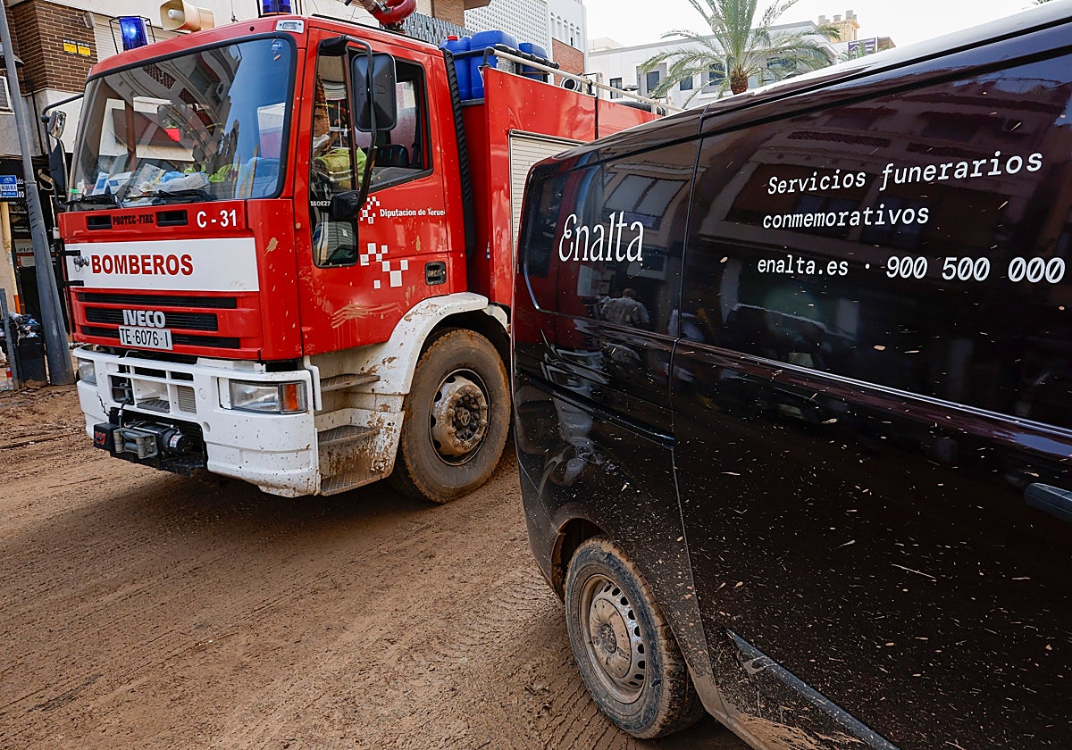Un camión de bomberos pasa junto a una furgoneta de los servicios funerarios por las calles de Catarroja, en Valencia