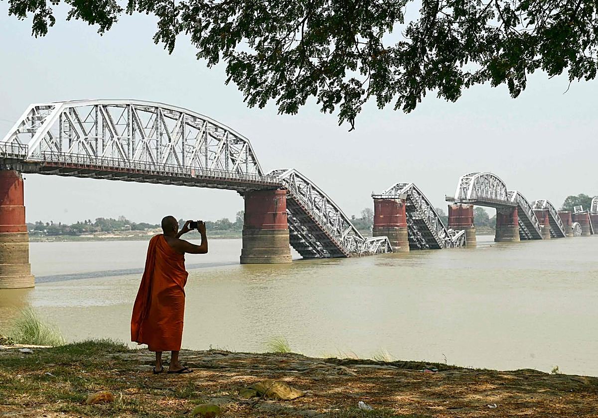Un monje hace una foto a orillas del río Irrawaddy, frente al derruido puente de Ava