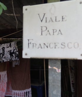 Imagen secundaria 2 - Oscar posa con su abuela Epifania y otros niños que viven en el Lido. Epifania guarda como un tesoro las fotos de las visitas de Francisco. A la derecha, la calle del Papa Francisco 