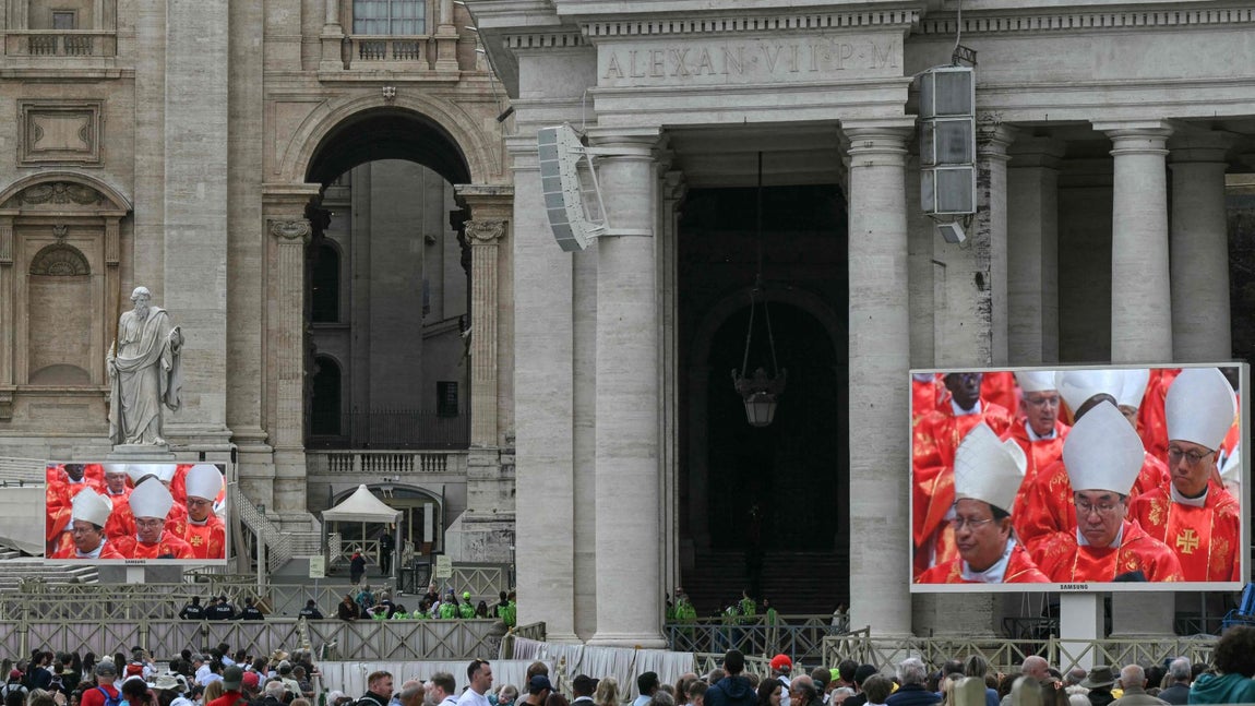Grupos de curiosos atienden la misa celebrada antes del inicio del cónclave en pantallas instaladas en la Plaza de San Pedro.