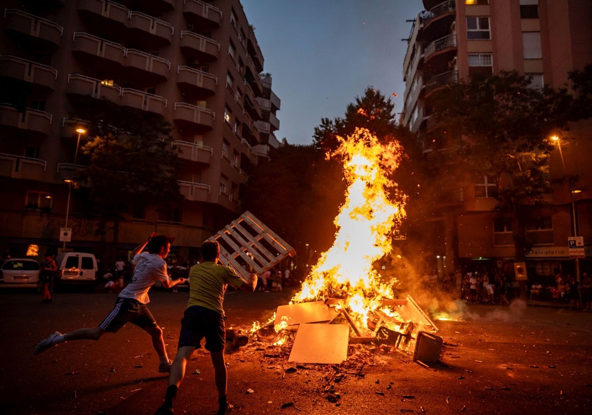 Dos chicos tiran un palé de madera a la hoguera del barrio de Sant Antoni, en Barcelona