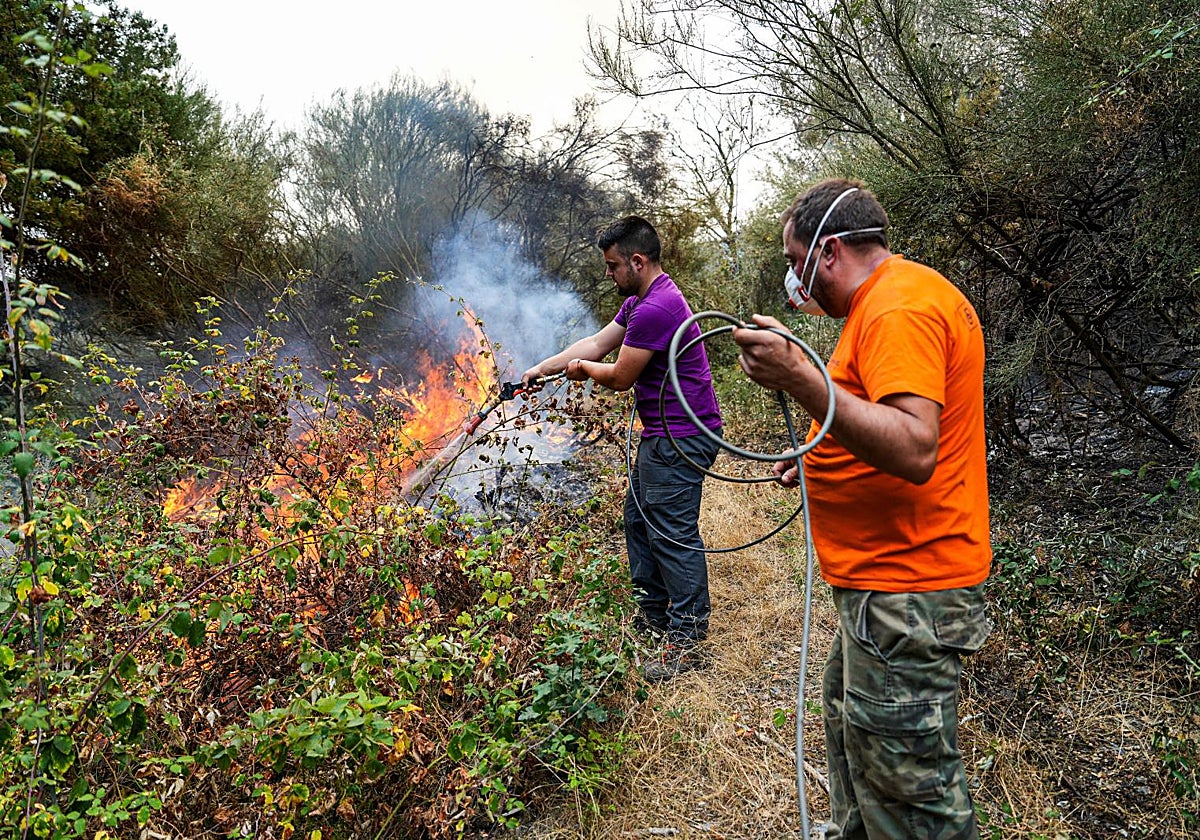 Vecinos intentan apagar el fuego con una manguera que se acerca a las casas en el monte leonés