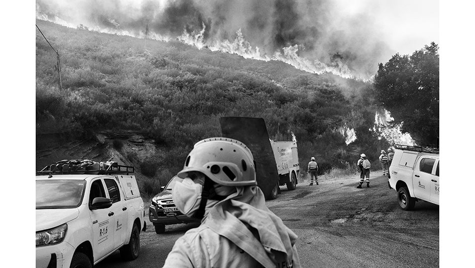Las llamas avanzan ladera abajo mientras los equipos de extinción se preparan para contener el frente desde la carretera. Entre el humo y el calor, los vehículos permanecen listos para dar apoyo y desplegar material. En este punto crítico, el objetivo era evitar que el fuego cruzara la carretera LE-4212. Si las llamas lo hubieran hecho, el incendio habría alcanzado dimensiones imposibles de controlar y habría arrasado los pueblos del valle de Fornela.