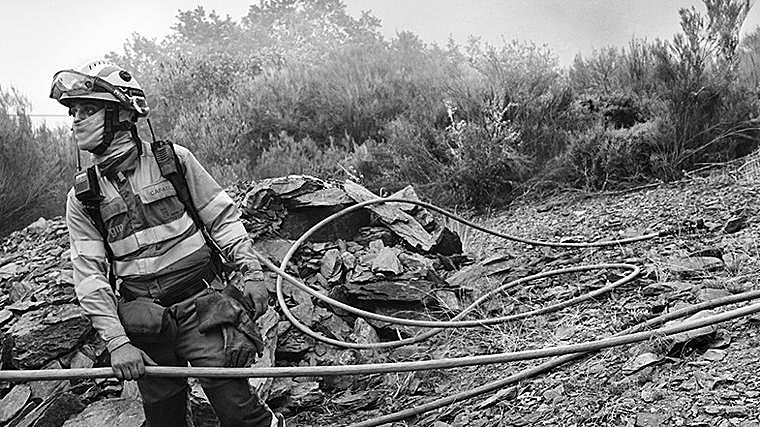 Peranzanes, Valle de Fornela, León. 19 de agosto de 2025. Un bombero sostiene una manguera mientras observa el avance del fuego en la ladera. El humo cubre parte del horizonte y convierte cada movimiento en una tarea lenta y vigilante. La tensión se refleja en la postura: preparado para actuar en cualquier momento.En el valle de Fornela, los equipos trabajaron durante horas en condiciones extremas para contener las llamas y evitar que alcanzaran los pueblos cercanos. La presión constante por mantener la línea de defensa fue clave para impedir que el incendio cruzara la carretera y arrasara todo el valle.