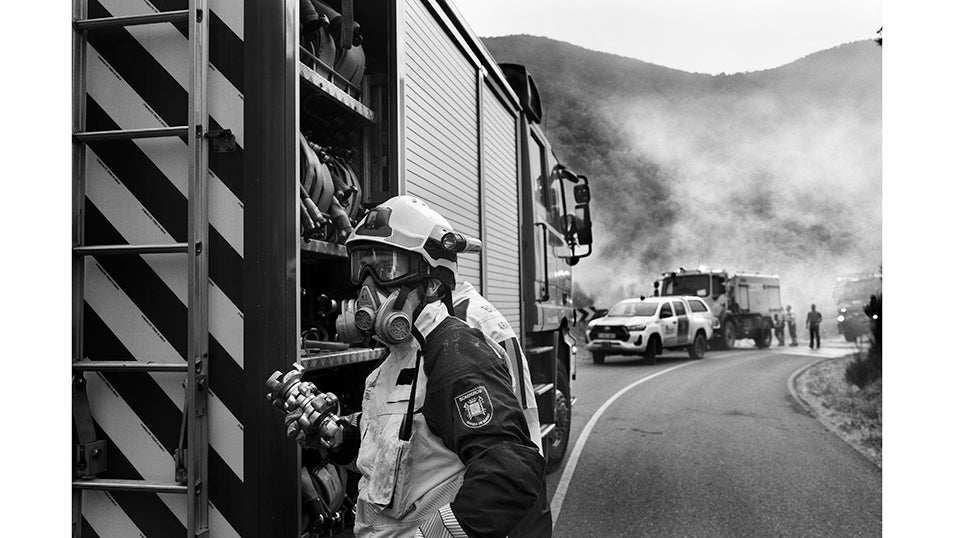 Un bombero revisa el material en el camión mientras el humo cubre la carretera. La máscara en su rostro refleja la dureza del ambiente. En la LE-4212 se concentró uno de los frentes más peligrosos. Allí, los equipos trabajaron sin descanso para impedir que el fuego cruzara al otro lado de la vía, lo que habría puesto en riesgo a todo el valle de Fornela.