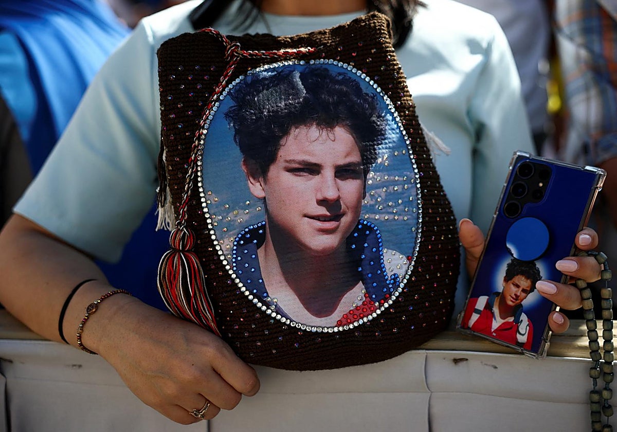 Una mujer lleva un bolso y un teléfono móvil con el rostro de Carlo Acutis