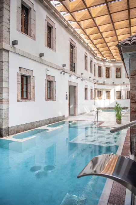 Escapada bienestar a Las Caldas by Blau Hotels en Asturias (desde 100 €, noche). Situado a 8 kms de Oviedo, combina lujo y descanso en un paraíso natural y junto a un manantial de aguas minero-medicinales. El manantial ofrece circuitos estimulantes y relajantes a través de espacios abovedados, piscinas de relajación, termas secas y de vapor, y todo ello presidido por la cueva de El Manantial, en la que brota, a 40ºC, el agua minero-medicinal. Además, el área wellnes & beauty cuenta con 25 cabinas donde disfrutar de una amplia gama de tratamientos.