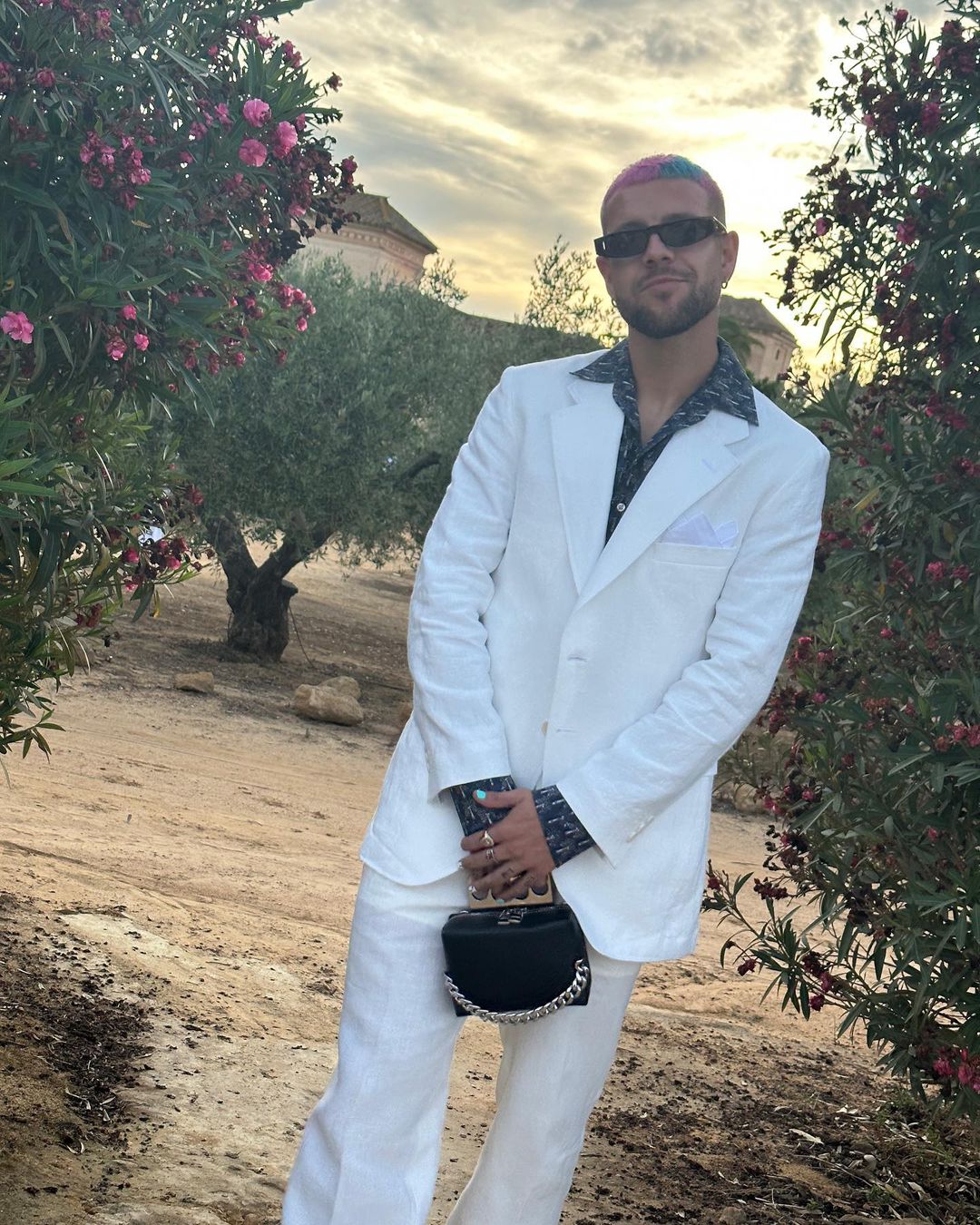 El futbolista del Betis Aitor Rubial posa durante una boda con un traje blanco y un bolso de mano de Alexander McQueen. Este clutch es solo uno de su amplia colección de bolsos de lujo. 