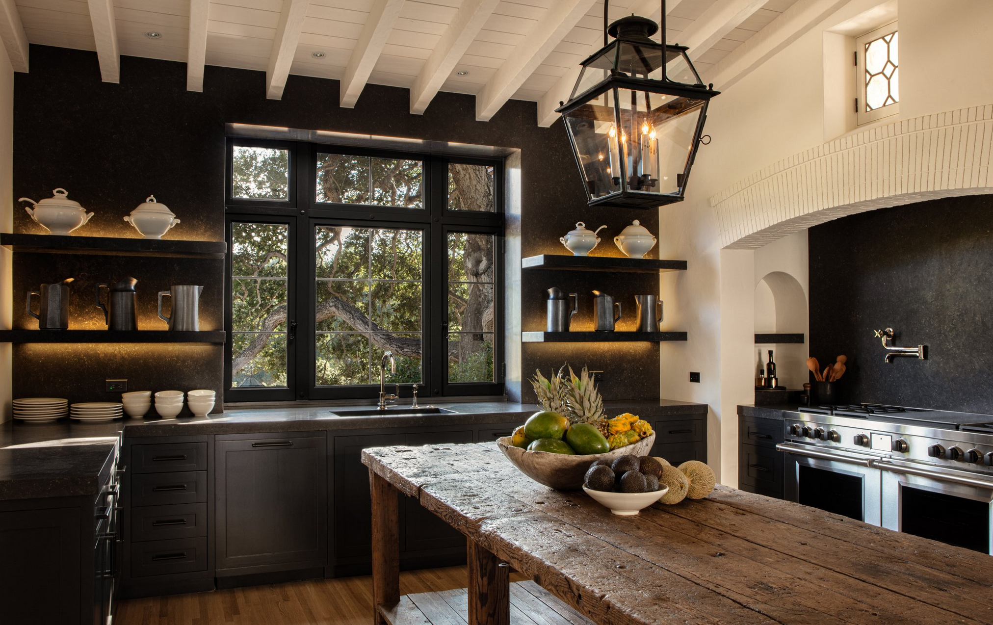 La cocina cuenta con gabinetes de madera en color oscuro, electrodomésticos de alta gama y una mesa de madera antigua en el centro