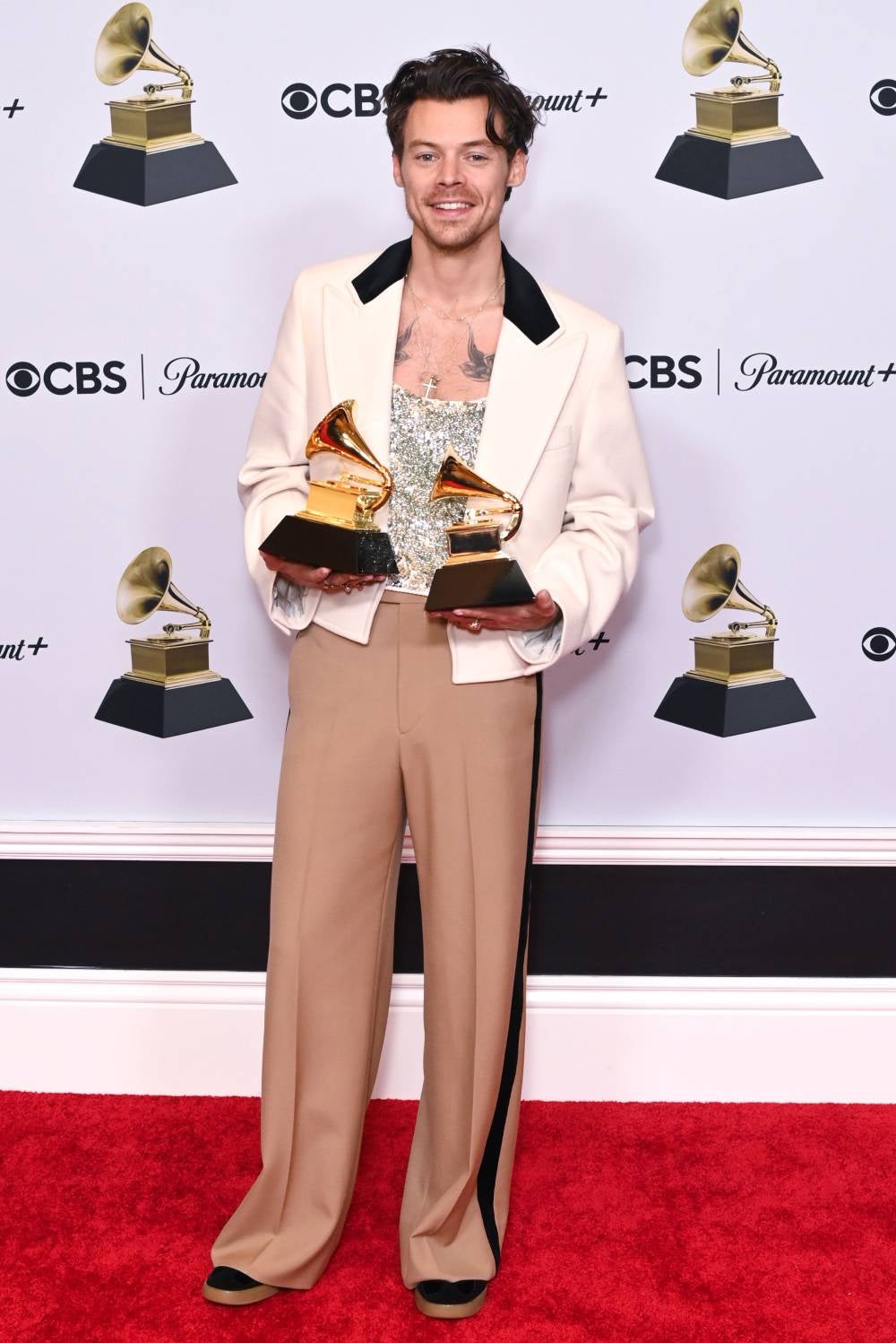 Cerramos el triplete de Harry Styles en los Grammy con su look que combina piezas retro con tendencia. Está compuesto por una chaqueta color marfil, unos pantalones camel y una camiseta de tirantes bordada con lentejuelas con la que recogió sus gramófonos en esta misma gala.