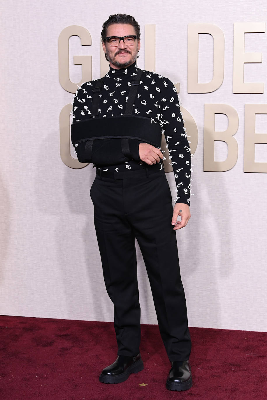 Pedro Pascal, que posó con el brazo en cabestrillo, eligió un pantalón sastre que combinó con jersey de cuello vuelto, en negro adornado con nudos blancos. Es un total look de Bottega Veneta. 