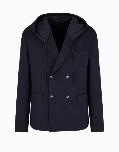 Una temporada más, Giorgio Armani Neve vuelve con una serie de actividades en espacios especialmente renovados para mostrar la colección de invierno. La colección de hombre se presenta con tonos densos de azul marino y chocolate, como esta blazer cruzada con solapas confeccionada en suave paño de mezcla de lana con trama diagonal. La prenda está equipada con una práctica capucha de nailon extraíble con cierre a presión. Precio: 610€