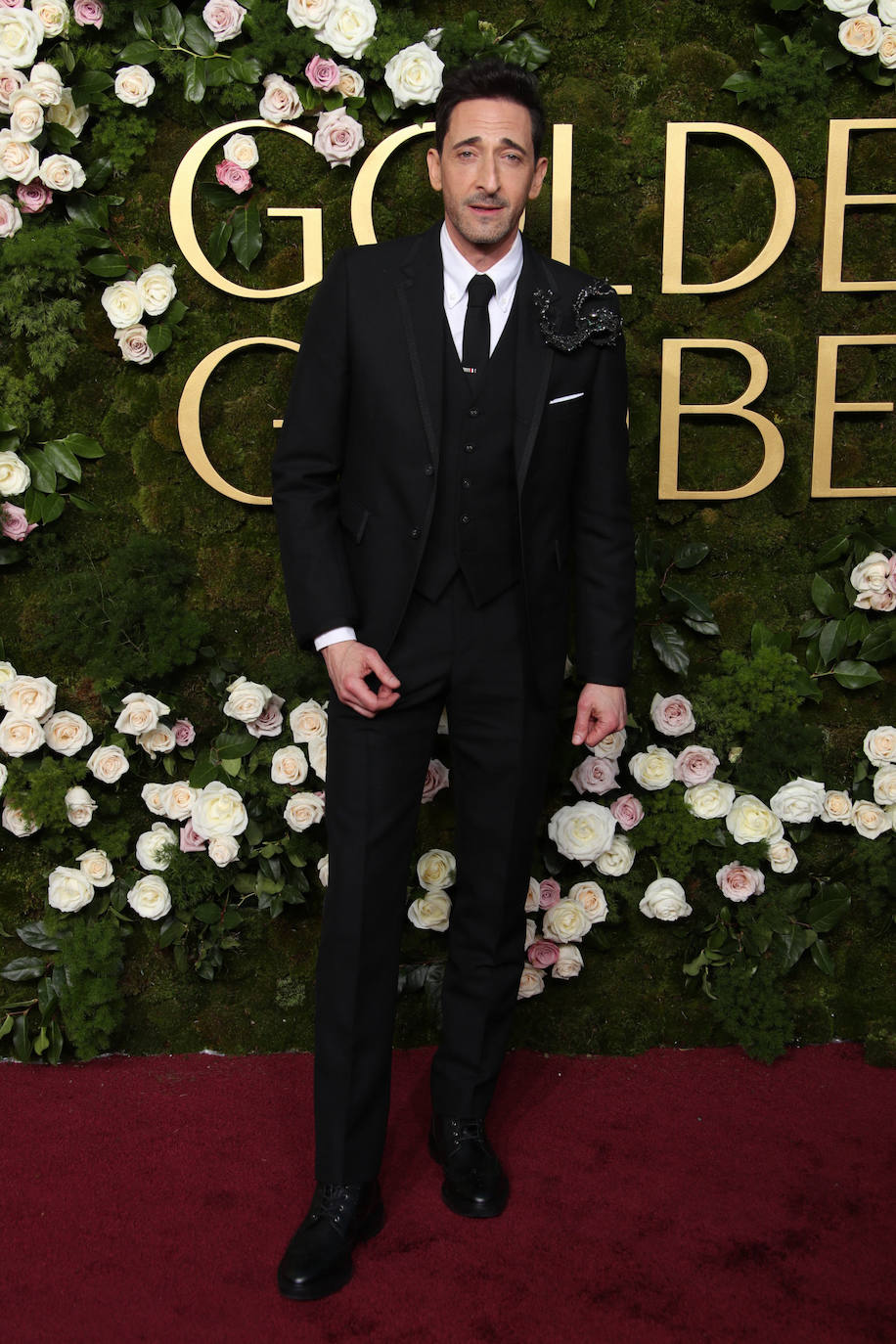 Adrien Brody con un traje de tres piezas adornado con un broche XXL. 