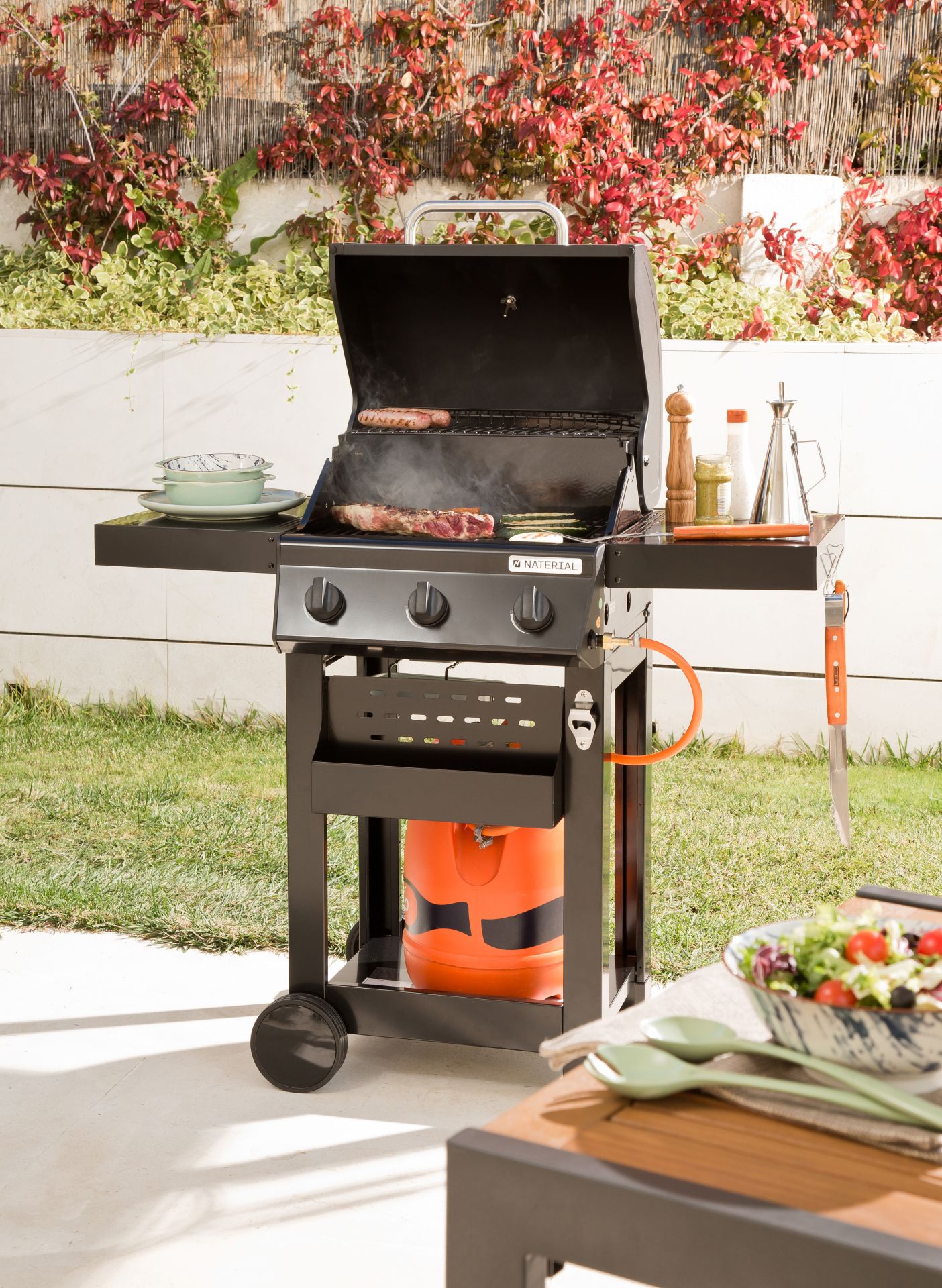 Se acerca el buen tiempo y con él las barbacoas. ¿Existe algún padre que no disfrute con este ritual? Sorpréndele con una de diseño como este modelo con de gas Naterial 3B Alton con función de grill, recomendada para 6 comensales. Está fabricada en acero esmaltado y texturizado de color negro. Cuenta con 3 quemadores de acero inoxidable con encendido piezoeléctrico de 9 kW y 2 parrillas de acero esmaltado con acabado brillante. Incluye carro con 2 ruedas grandes para facilitar su transporte, tapa de cocción de acero esmaltado y galvanizado con termómetro integrado para controlar en todo momento la temperatura de los alimentos. También dispone de abrebotellas, 2 mesas abatibles laterales para poner los productos y facilitar el manejo y 3 ganchos para tener a mano los utensilios de cocina. Su precio es de 199 euros