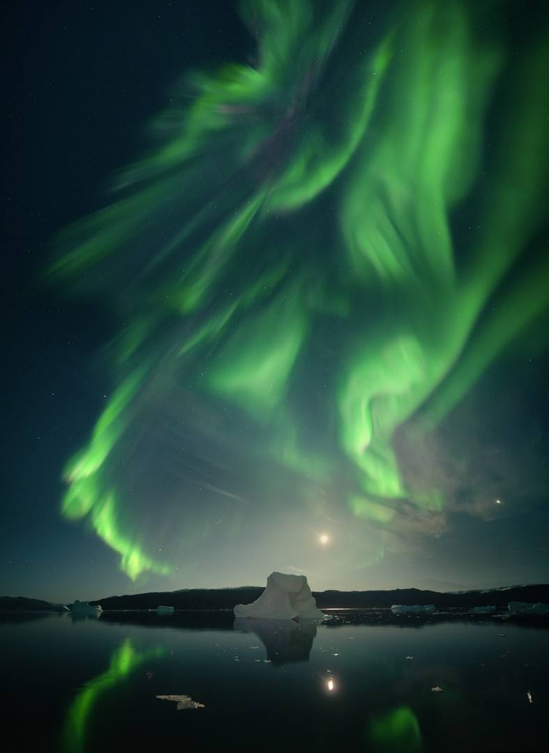 'Towering Ice'. Foto tomada en Scoresby Sund, Groenlandia. "Towering Ice fue captada desde un rompehielos, lo que significa que el tiempo de exposición tuvo que ser bastante corto para evitar el movimiento del barco a la deriva y el balanceo. La Aurora estalló sobre nuestras cabezas, lo que también requirió una velocidad de obturación más rápida, permitiéndome congelar su movimiento".