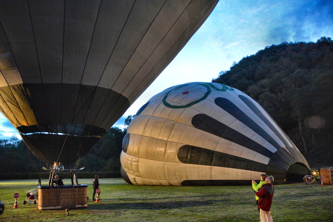 Con las primeras luces del alba se procede al inflado de las velas. La compañía Vol de Coloms (https://www.voldecoloms.cat/es/), que ofrece la experiencia única de sobrevolar en globo estos volcanes, nació a principios de los años 90 del siglo pasado de una idea de cuatro hermanos apellidados Colom. Curiosamente Vol de Coloms podría traducirse por Vuelo de Palomas. Hay que pegarse un buen madrugón, pero merece la pena. Los vuelos en globo se realizan solo en las mejores condiciones atmosféricas y a primera hora de la mañana es cuando el viento suele estar más calmado. Si la velocidad del aire sobrepasa los 15 km. por hora; si hay tormenta o helada, el vuelo se suspende.